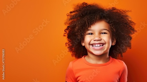 A cute little boy stands smiling on an orange background. A happy child, the concept of joy, surprise. © Cherkasova Alie