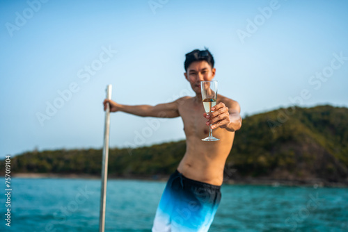 A man in a bathing suit is holding a glass of wine while standing on a boat in t