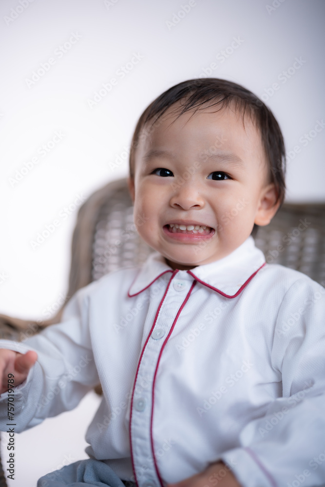 A young child is sitting in a wicker chair with a smile on his face. The chair is placed on a white background, and the child is holding a blanket in his lap. Concept of warmth and comfort A young child is sitting in a wicker chair with a smile on his face. The chair is placed on a white background, and the child is holding a blanket in his lap. Concept of warmth and comfort
