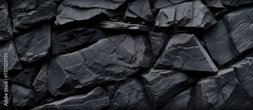 A close up of a stack of dark automotive tires, resembling black rocks. The monochrome photography highlights the grey pattern on the rubber, creating a dark and metallike appearance