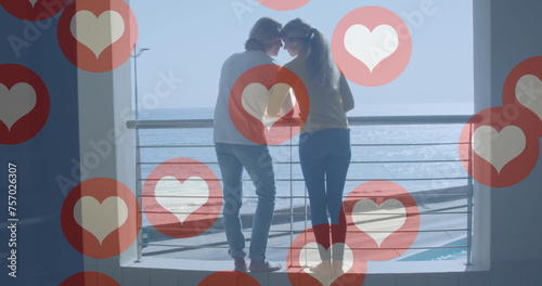 Image of social media heart icons over happy couple on balcony by seaside