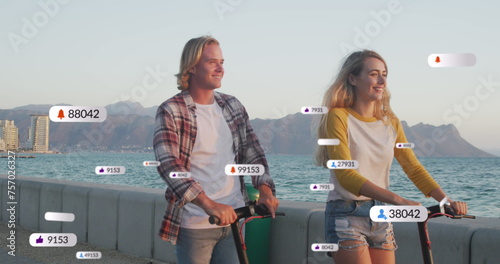 Image of social media notifications over smiling couple using scooters on holiday by the sea
