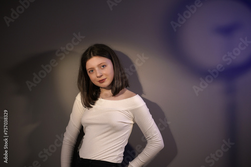 Portrait of a pretty cute girl on a gray background in the studio. Brunette girl looks at the camera. Beautiful female model posing in studio in light flashes. © Andrii