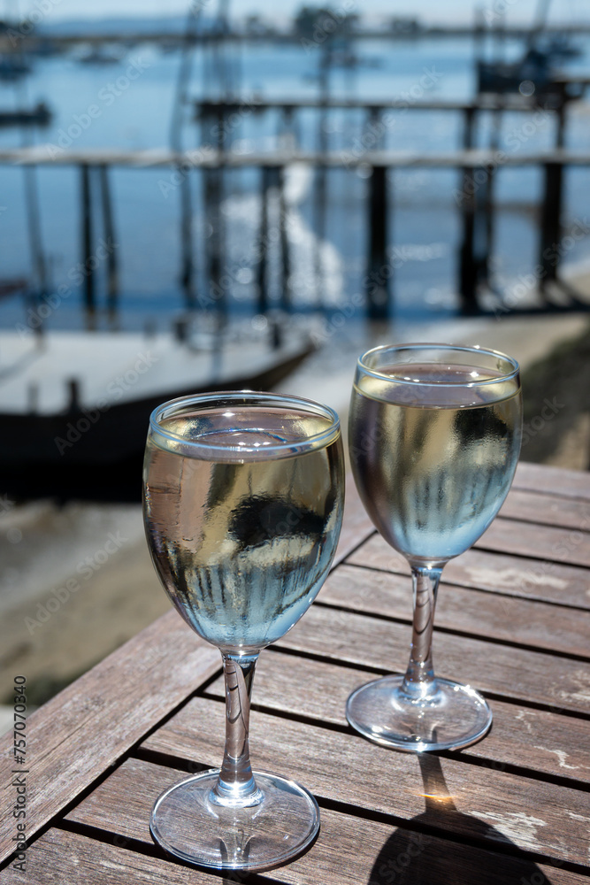 Obraz premium Drinking of white wine at farm cafe in oyster-farming village, with view on boats and water of Arcachon bay, Cap Ferret peninsula, Bordeaux, France