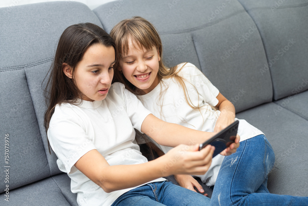 Child with smartphone at home. Two kids using smart phone, surfing internet or using social media. Two kids using online mobile phone, call, watching content, playing video games, sitting on couch Child with smartphone at home. Two kids using smart phone, surfing internet or using social media. Two kids using online mobile phone, call, watching content, playing video games, sitting on couch