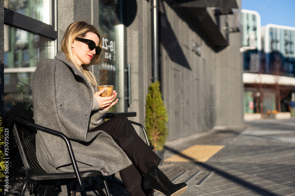Young woman enjoying a coffee, sitting with mobile phone on the cafe terrace on the old city street during a sunny day