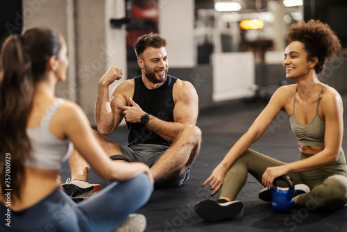 Three sporty friends sitting on a gym floor and showing muscles during a break.