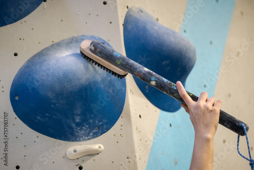 Hand holding big brush on long stick in bouldering climbing gym brushing off chalk of a large hold for the hands