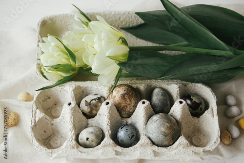 Happy Easter! Stylish easter eggs in tray and tulips on rustic table with linen cloth.  Modern natural dye marble eggs with spring flowers still life. Top view © sonyachny