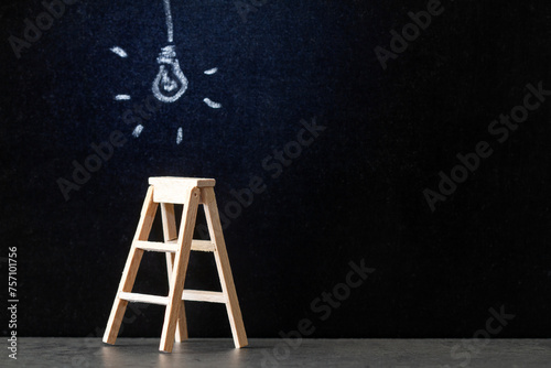 Wooden ladder with glowing light bulb drawn with chalk on blackboard, concept of new ideas, innovations and solutions in business