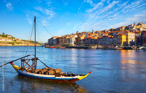 Old town of Porto, Portugal. Antique boat with port wine barrels on the water Douro River. Sunny day over silhouettes skyline roofs houses along river.