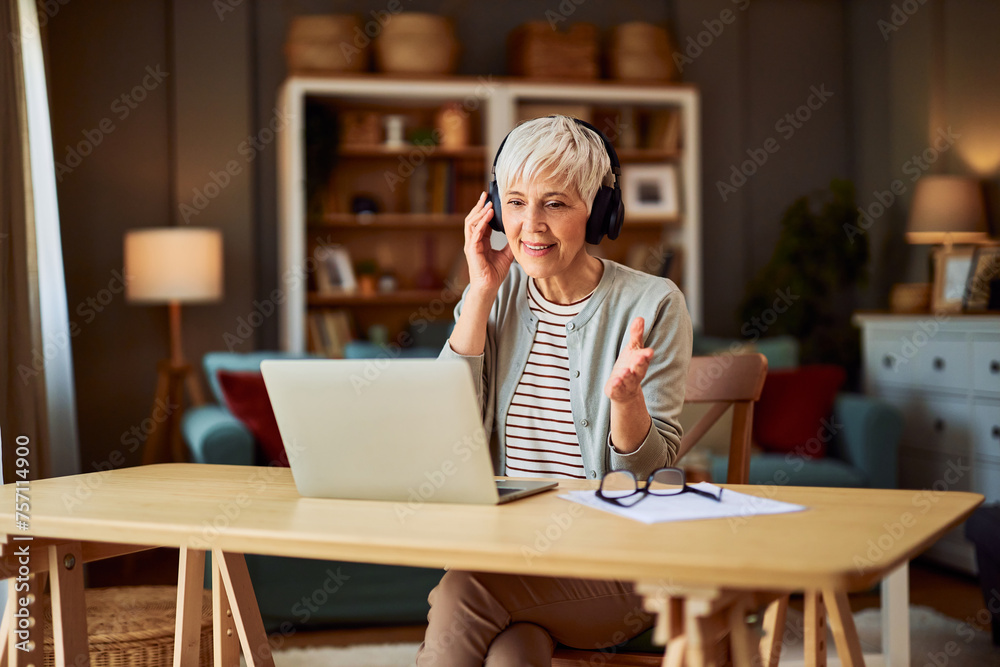 A dedicated senior adult woman wearing headphones and having a video call on her laptop while working from home A dedicated senior adult woman wearing headphones and having a video call on her laptop while working from home