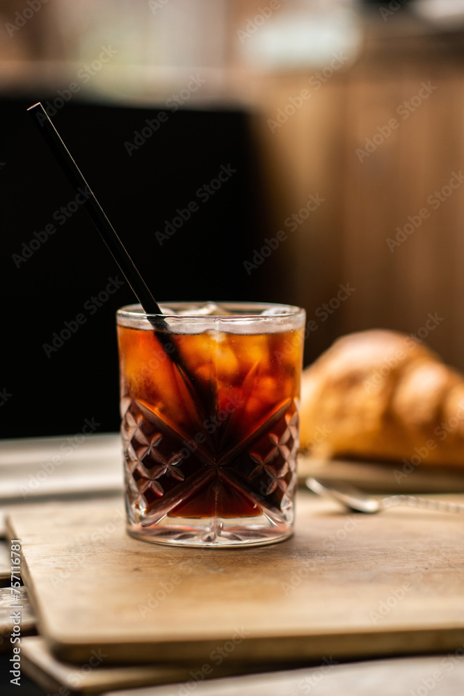 Glass of iced coffee with a pastry on coffee shop table. Cold summer drink on a wooden background. Glass of iced coffee with a pastry on coffee shop table. Cold summer drink on a wooden background.