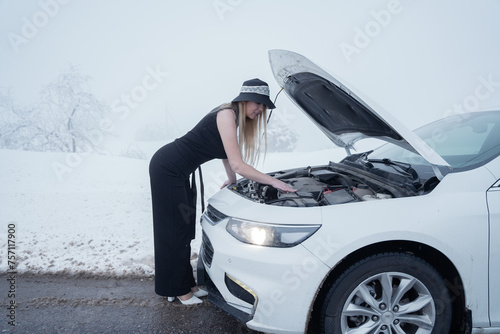 Woman in winter clothing checking under car hood on a snowy road © Юля Чиви