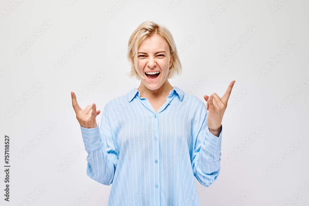 Joyful young woman in blue shirt making rock and roll hand gesture, laughing on white background. Joyful young woman in blue shirt making rock and roll hand gesture, laughing on white background.
