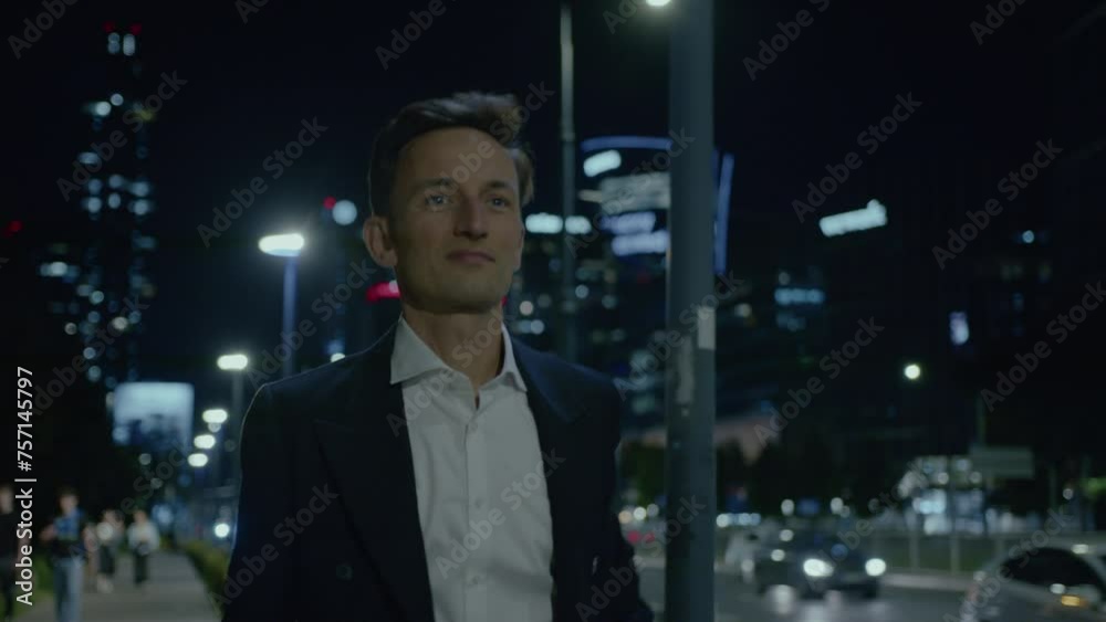 Suited man walks on city street at night and fixes hair, close frontal Suited man walks on city street at night and fixes hair, close frontal