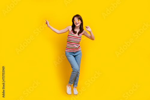 Full body photo of satisfied optimistic girl wear striped tank denim trousers dancing at summer party isolated on yellow color background