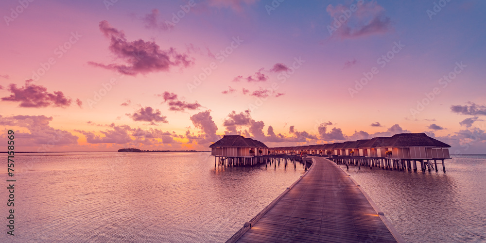 Amazing sunset panorama at Maldives. Luxury resort villas seascape with soft led lights under colorful sky. Beautiful twilight sky and dreamy clouds. Majestic beach background for vacation holiday