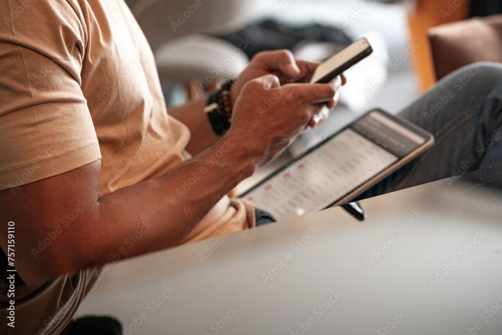 Close up of a young black man using mobile in living room and texting massages to colleague