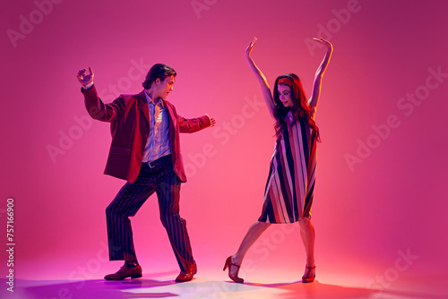 Young man and woman in stylish clothes dancing retro dance, boogie woogie against pink background in neon light. Concept of hobby, dance class, party, 50s, 60s culture, youth photo