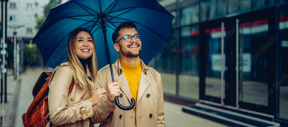 Happy young couple standing under an umbrella and looking around the city. Happy young couple standing under an umbrella and looking around the city.