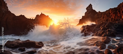 At dusk, a picturesque sunset illuminates the sky with hues of orange and pink over a rocky beach. Waves crash against the rocks, creating a mesmerizing atmosphere