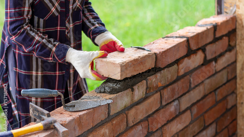 A young female bricklayer builds a wall, puts a brick on a cement mortar