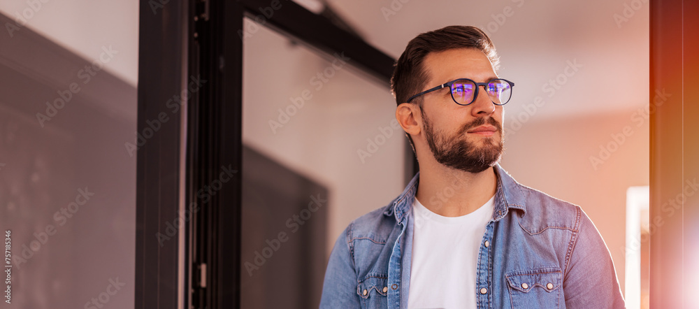 © kerkezz - Cheerful entrepreneur in denim shirt, wearing glasses, standing in his office in the morning. © kerkezz - Cheerful entrepreneur in denim shirt, wearing glasses, standing in his office in the morning.