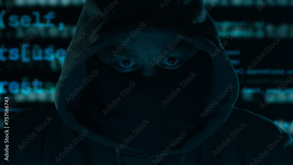 Hacker's Gaze Amidst Digital Chaos. Hooded figure with a masked face, program code in the background in a dark setting. Hacker's Gaze Amidst Digital Chaos. Hooded figure with a masked face, program code in the background in a dark setting.