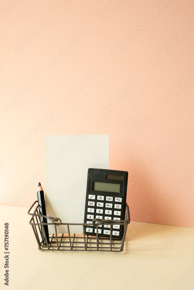 Consumer shopping basket with calculator, pencil, memo pad on ivory and pink background. Economic Concept