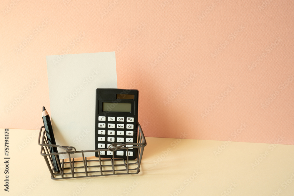 Consumer shopping basket with calculator, pencil, memo pad on ivory and pink background. Economic Concept