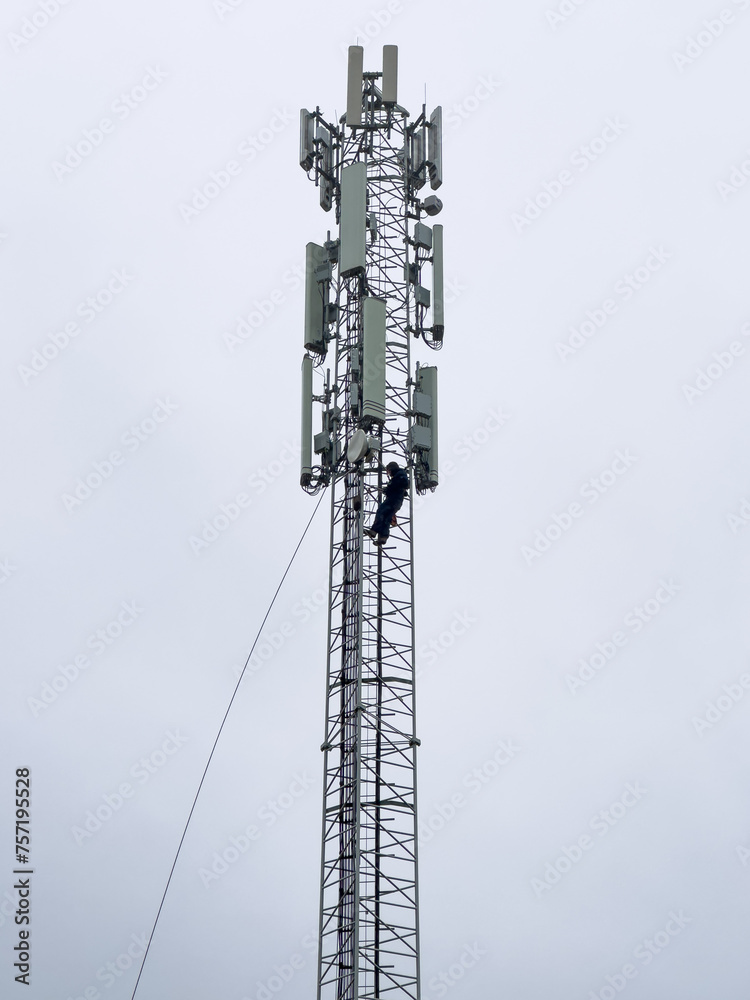 Mobile telecommunication cell tower with repairman, technician, climbing high doing maintenance. Person tethered