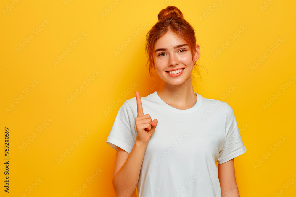 Portrait of a young girl points her finger up on a yellow background. Copy space Portrait of a young girl points her finger up on a yellow background. Copy space