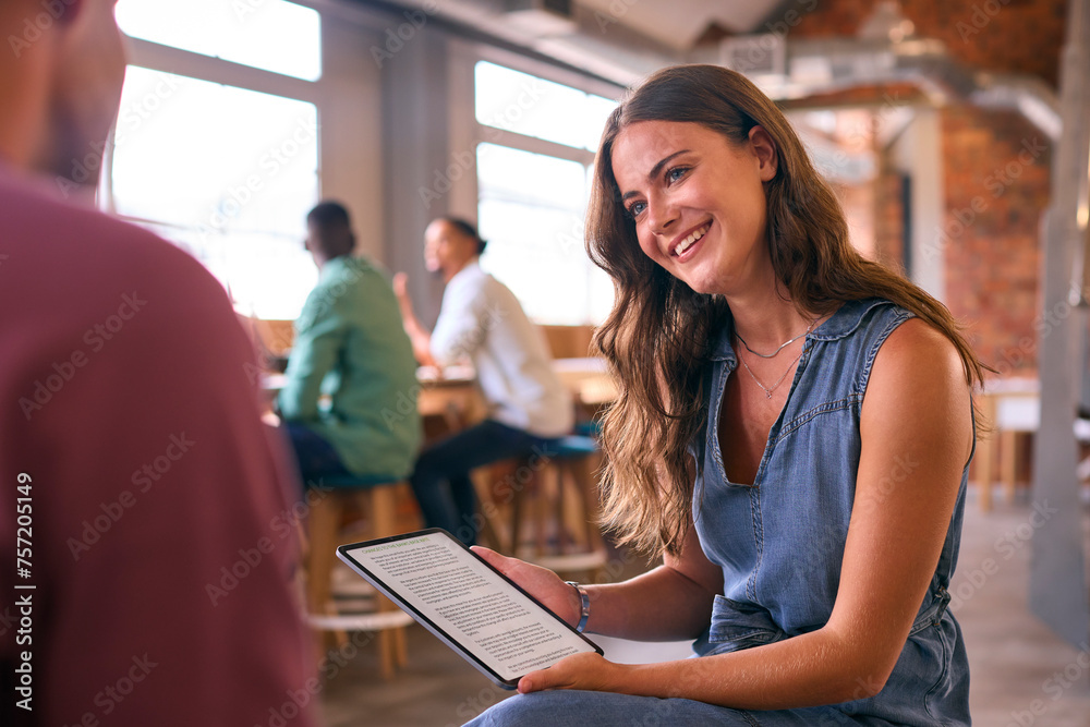 Two Young Businesspeople With Digital Tablet Meeting In Office With Colleagues In Background Two Young Businesspeople With Digital Tablet Meeting In Office With Colleagues In Background