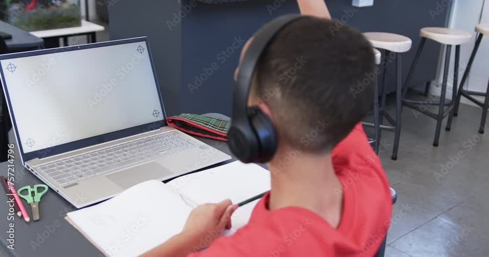 Biracial boy with headphones studies at a laptop in a classroom in school with copy space Biracial boy with headphones studies at a laptop in a classroom in school with copy space
