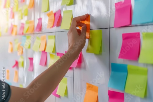 Close-up of hands young marketing woman engaged in a brainstorming session, using colorful sticky notes on a white wall to organize their Ideas, Goals, Objectives, Plans and Strategies in office.