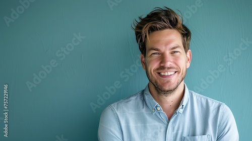 A man in casual attire looking directly at the camera with a genuine smile, set against a cool blue background