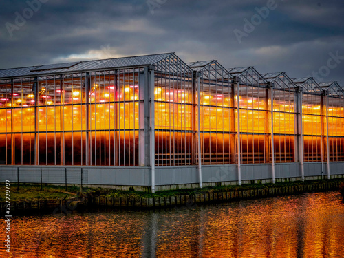 Glaring sunset behind a colossal greenhouse reflects on waterfront