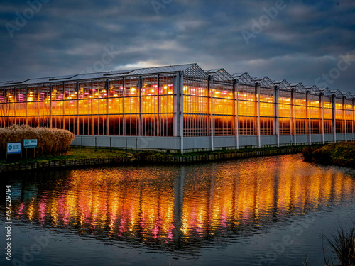 A greenhouse glows warmly at dusk, its light reflecting on the water photo