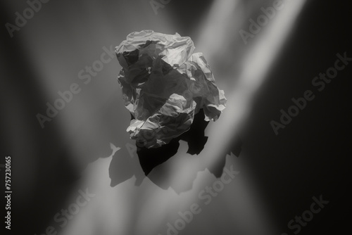 A crumpled piece of paper suspended in a void, with light casting dramatic shadows photo
