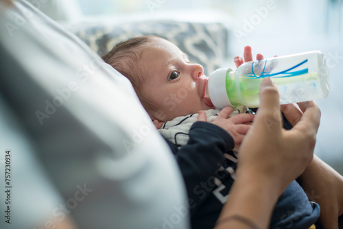 Infant being fed from a bottle by an adult's caring hands photo