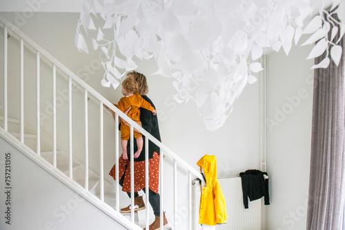 A child ascending a bright staircase, pausing to look upwards at a whimsical hanging decoration. photo