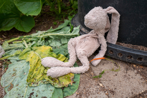 A lonely stuffed bunny slumped on the ground beside a wilting leaf. photo