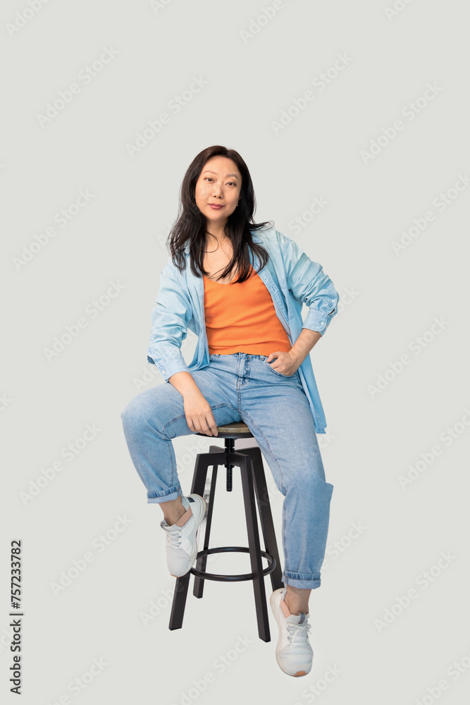 Photo portrait full body view of Asian woman sitting on bar stool isolated on grey background