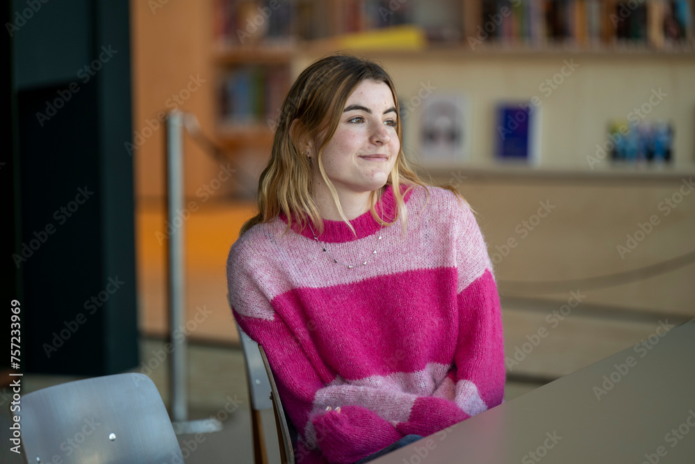Young woman smiling while sitting in a brightly lit library Young woman smiling while sitting in a brightly lit library