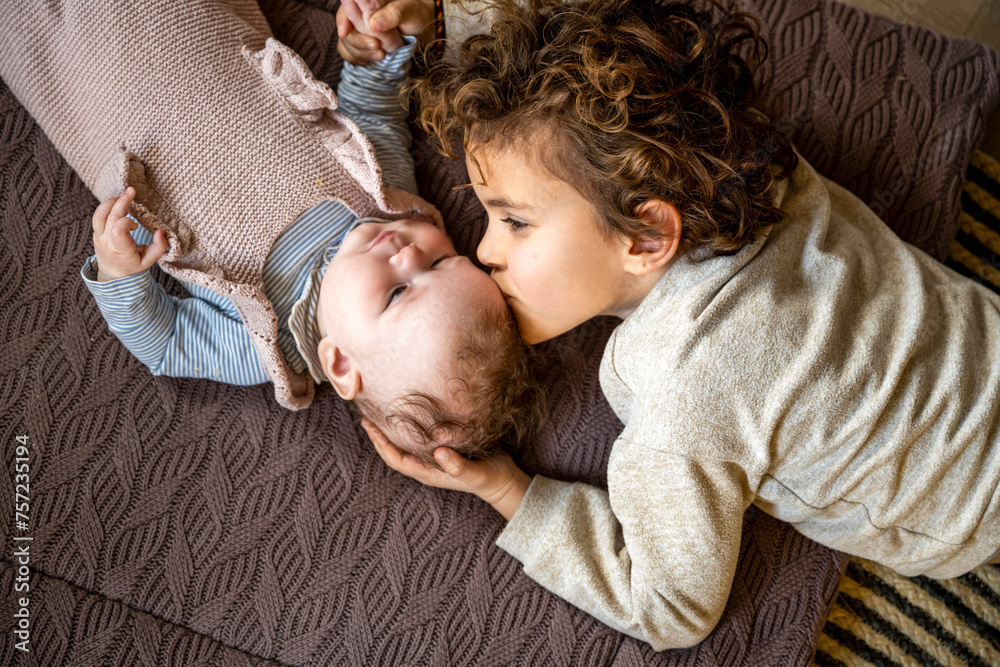 A tender moment as a young child gives a gentle kiss to a baby resting on a cozy blanket. A tender moment as a young child gives a gentle kiss to a baby resting on a cozy blanket.