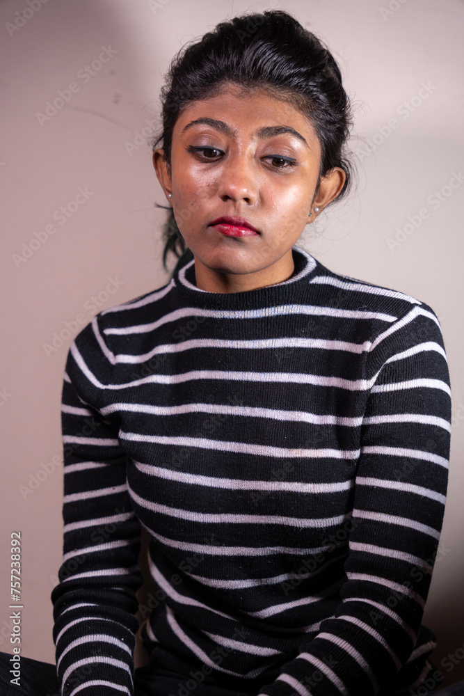 Fototapeta premium A woman with black and white stripes on her shirt is sitting on the floor. She has red lipstick on her lips and a serious expression on her face