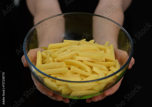 Miska z surowymi żółtymi ziemniakami pokrojonymi w słupki na frytki trzymana w dłoniach 
