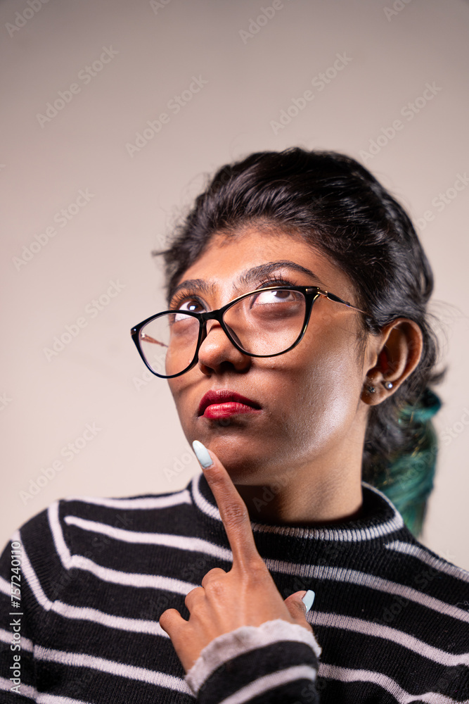 A woman with glasses is looking at the camera and pointing her finger. She has red lipstick on and her hair is pulled back. Concept of curiosity and contemplation