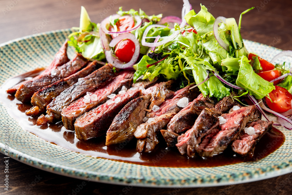steak cooked to a medium-rare level and is garnished with salt flakes and herbs. Adjacent to the steak is a fresh salad consisting of green lettuce leaves, sliced onions, and halved cherry tomatoes.